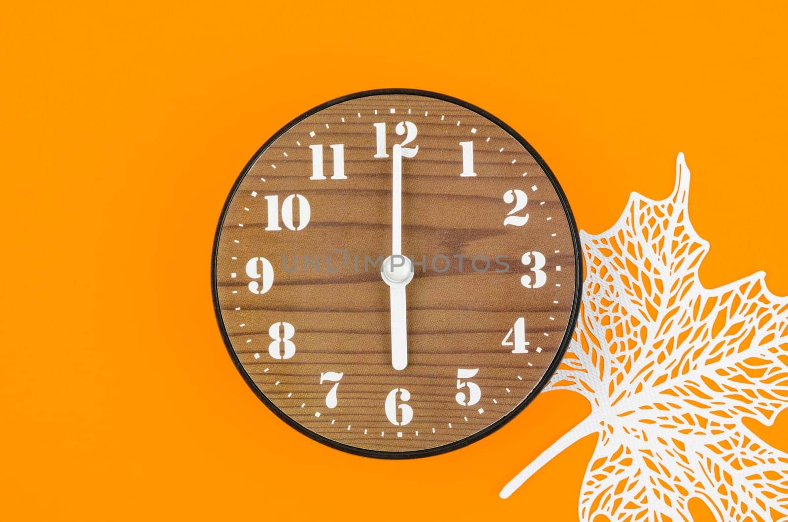 Wooden clock and paper maple leaf on a red background.
