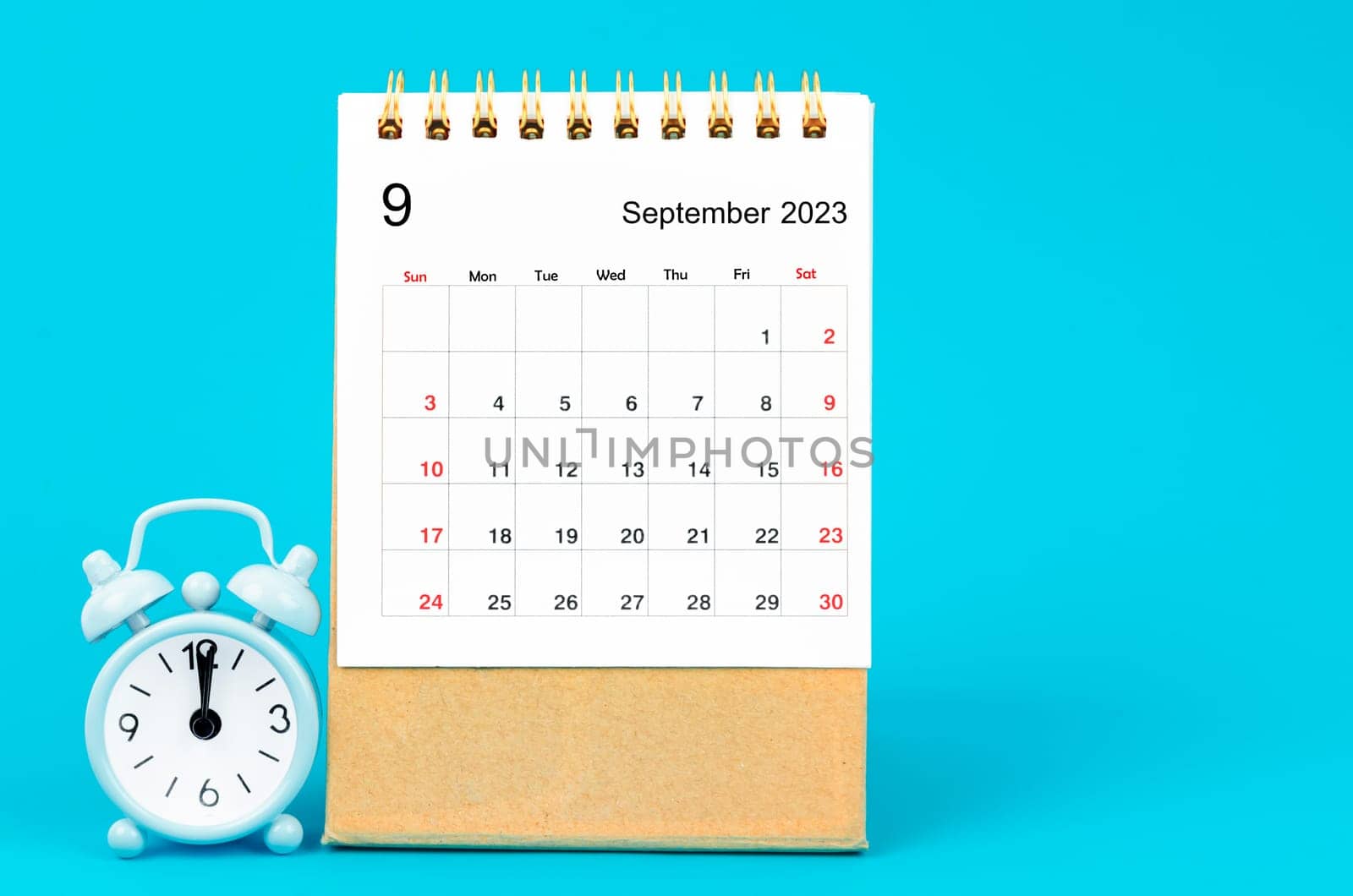 The September 2023 Monthly desk calendar for 2023 year and alarm clock on blue background. by Gamjai