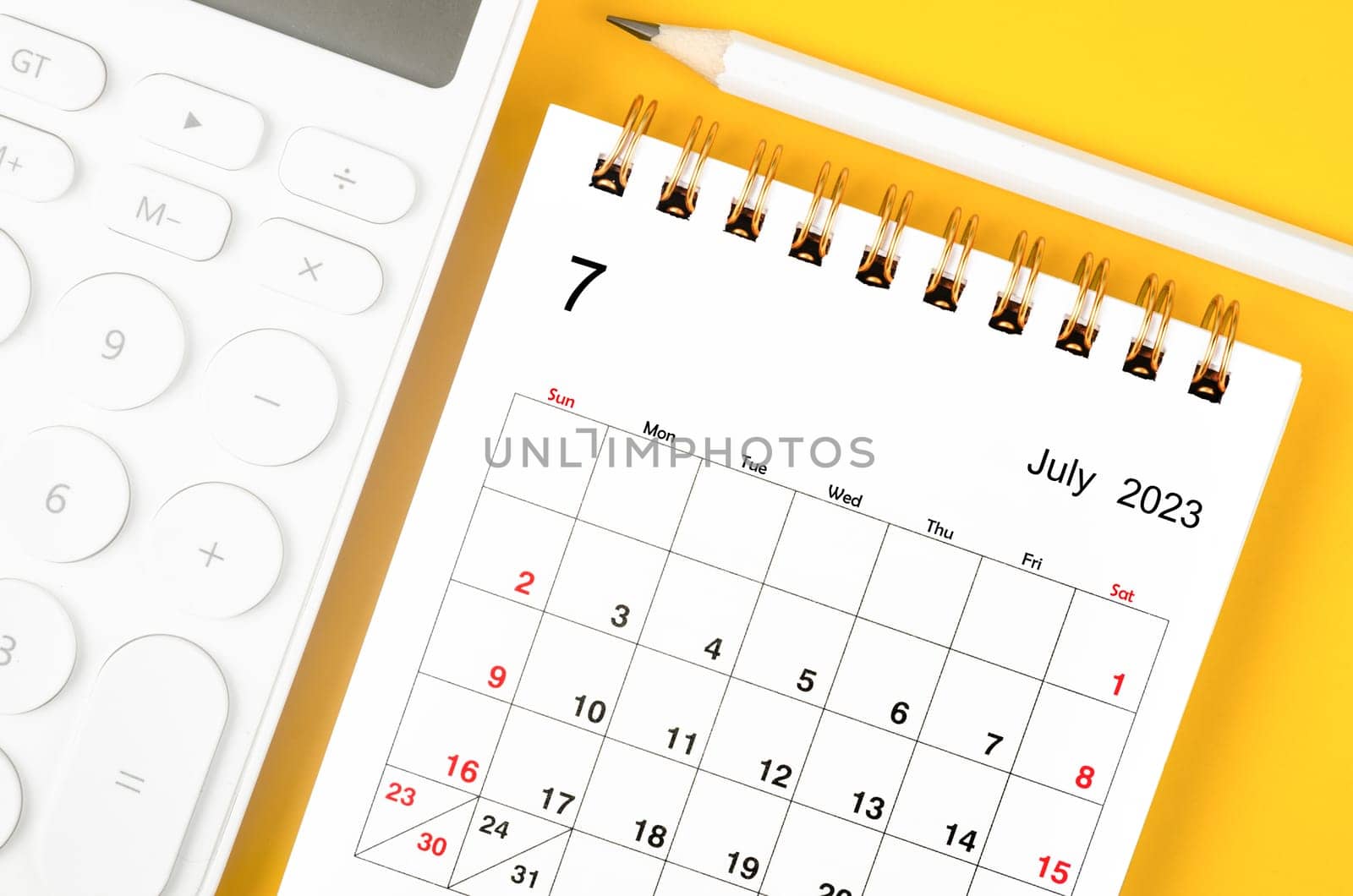 The July 2023 Monthly desk calendar for 2023 year and calculator with pen on yellow background. by Gamjai