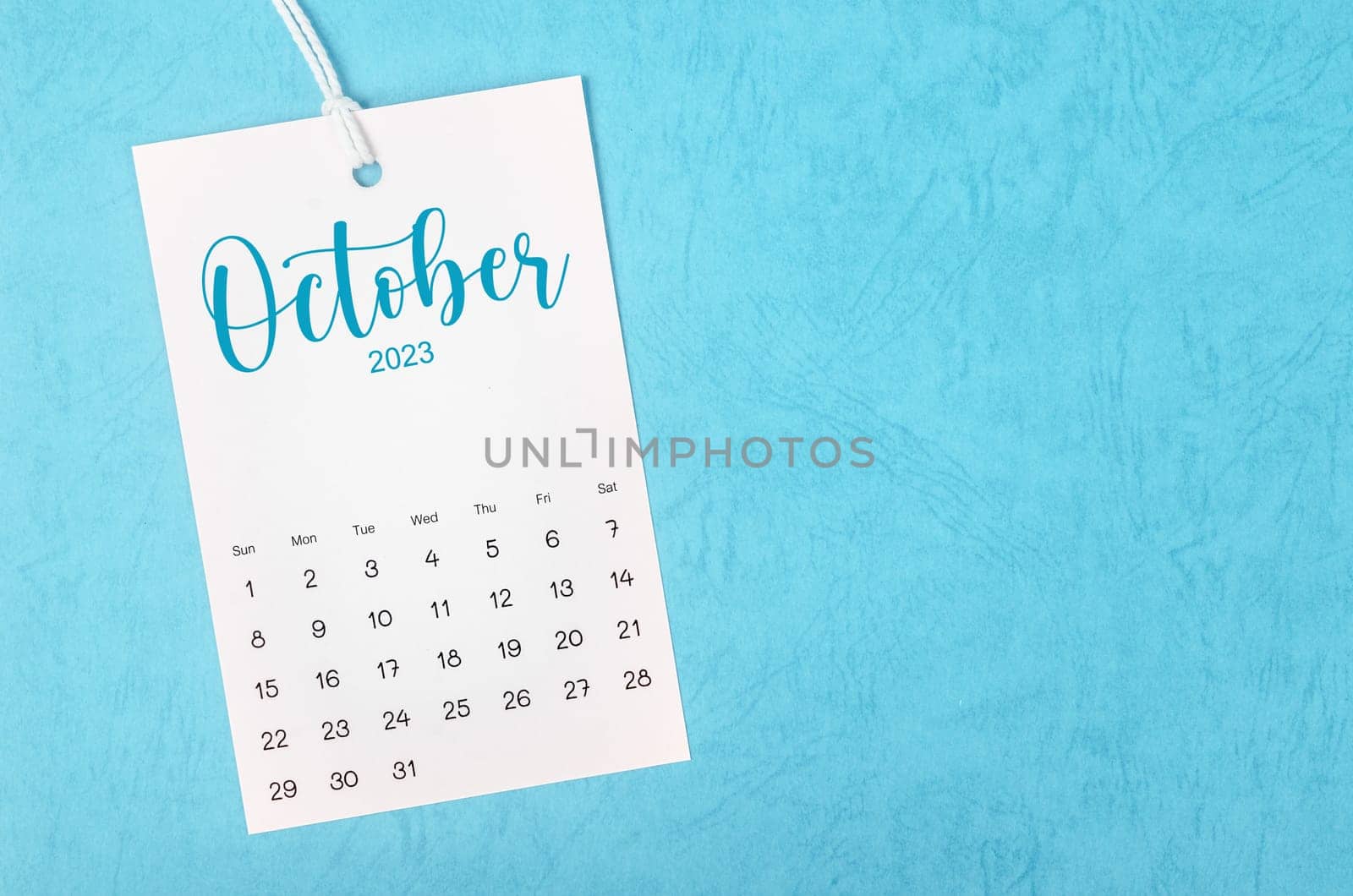 2023 October calendar page hanged on white rope on blue background.