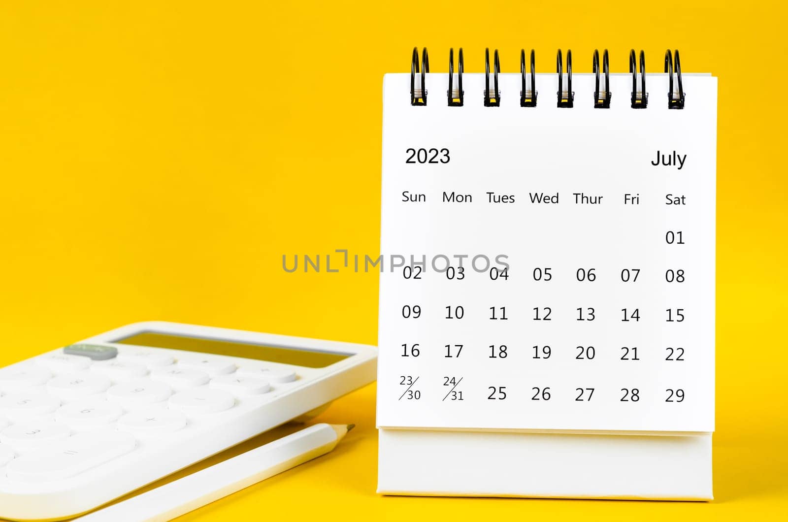 July 2023 Monthly desk calendar for 2023 year and calculator with pen on yellow background.