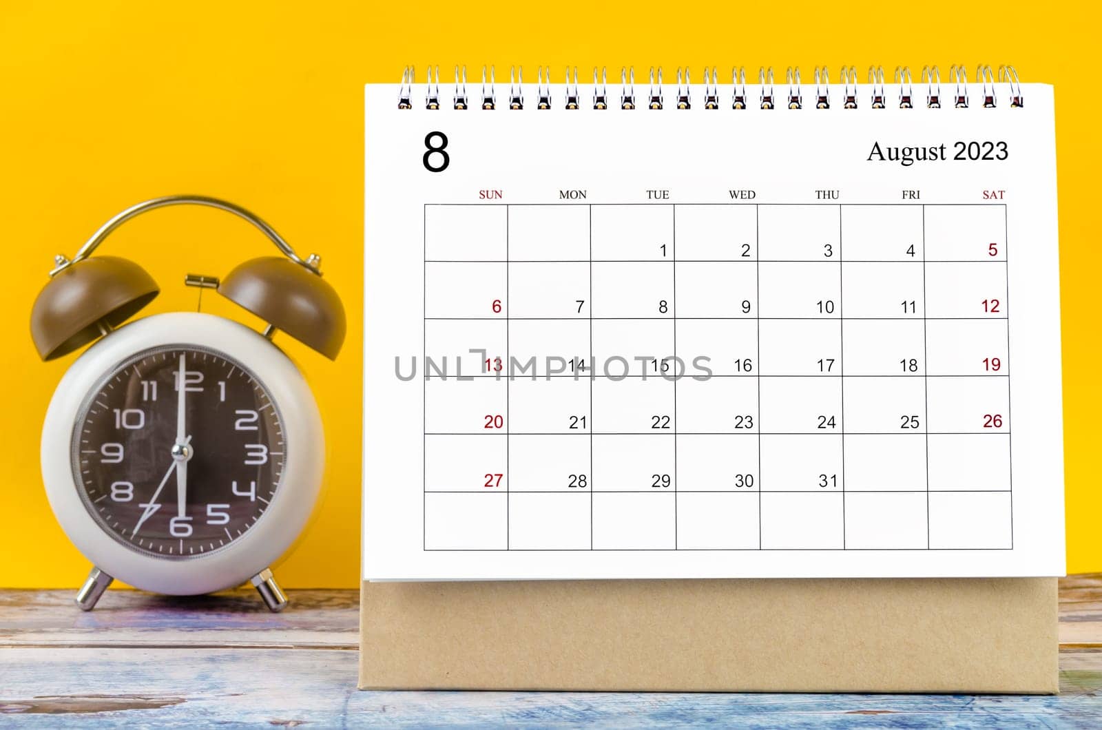 The August 2023 Monthly desk calendar for 2023 year and alarm clock. by Gamjai