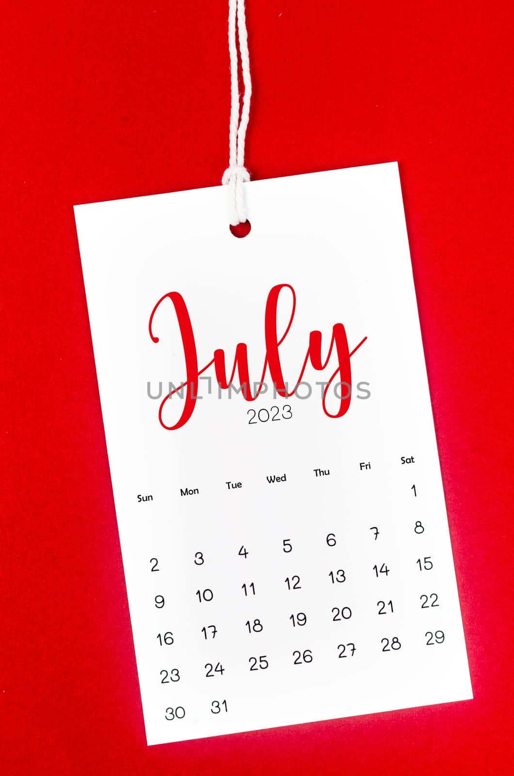 July 2023 calendar page for 2023 year hanged on white rope on Red background.