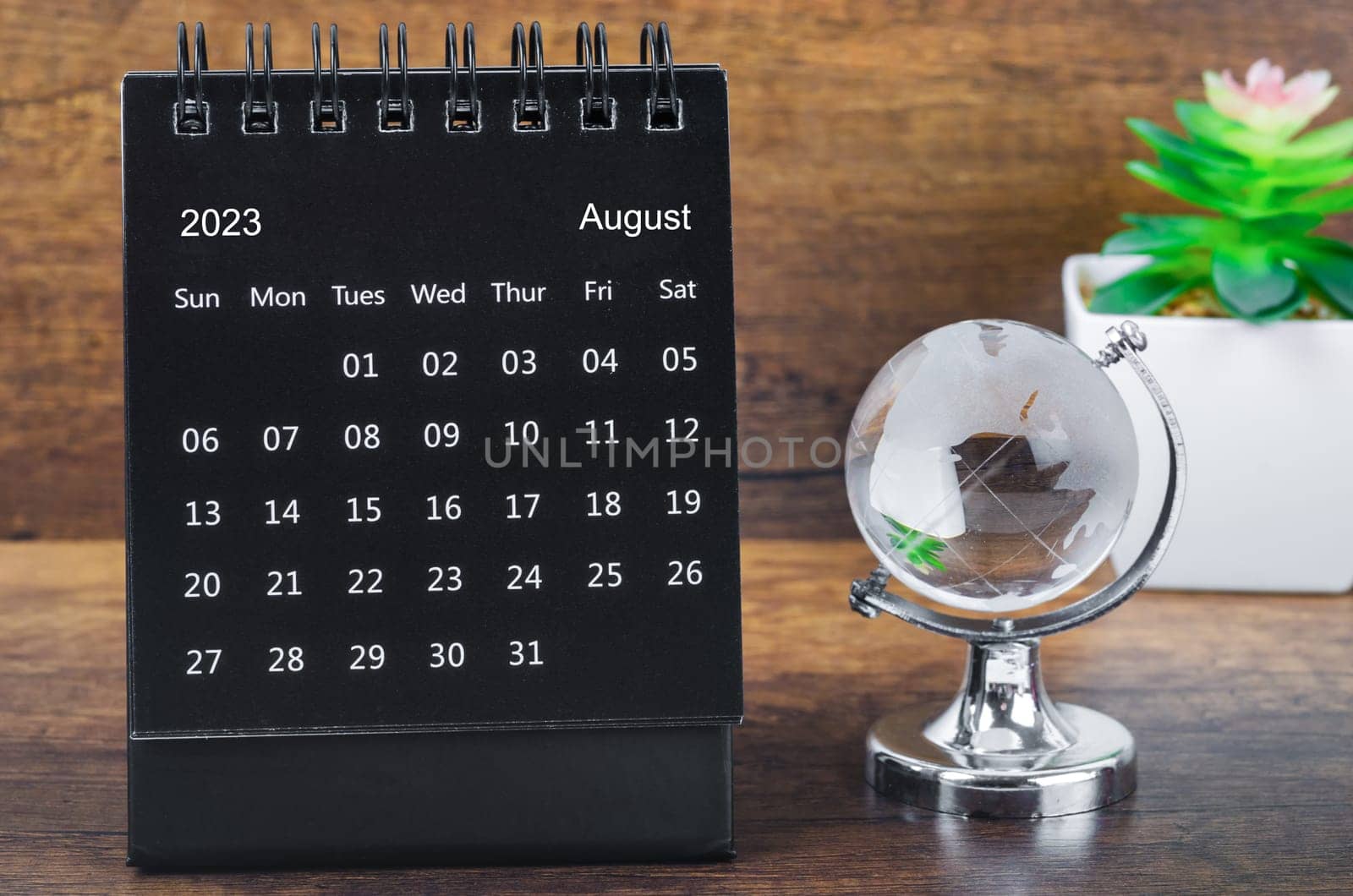 August 2023 desk calendar for 2023 year Black color with a crystal globe against a wooden table background.