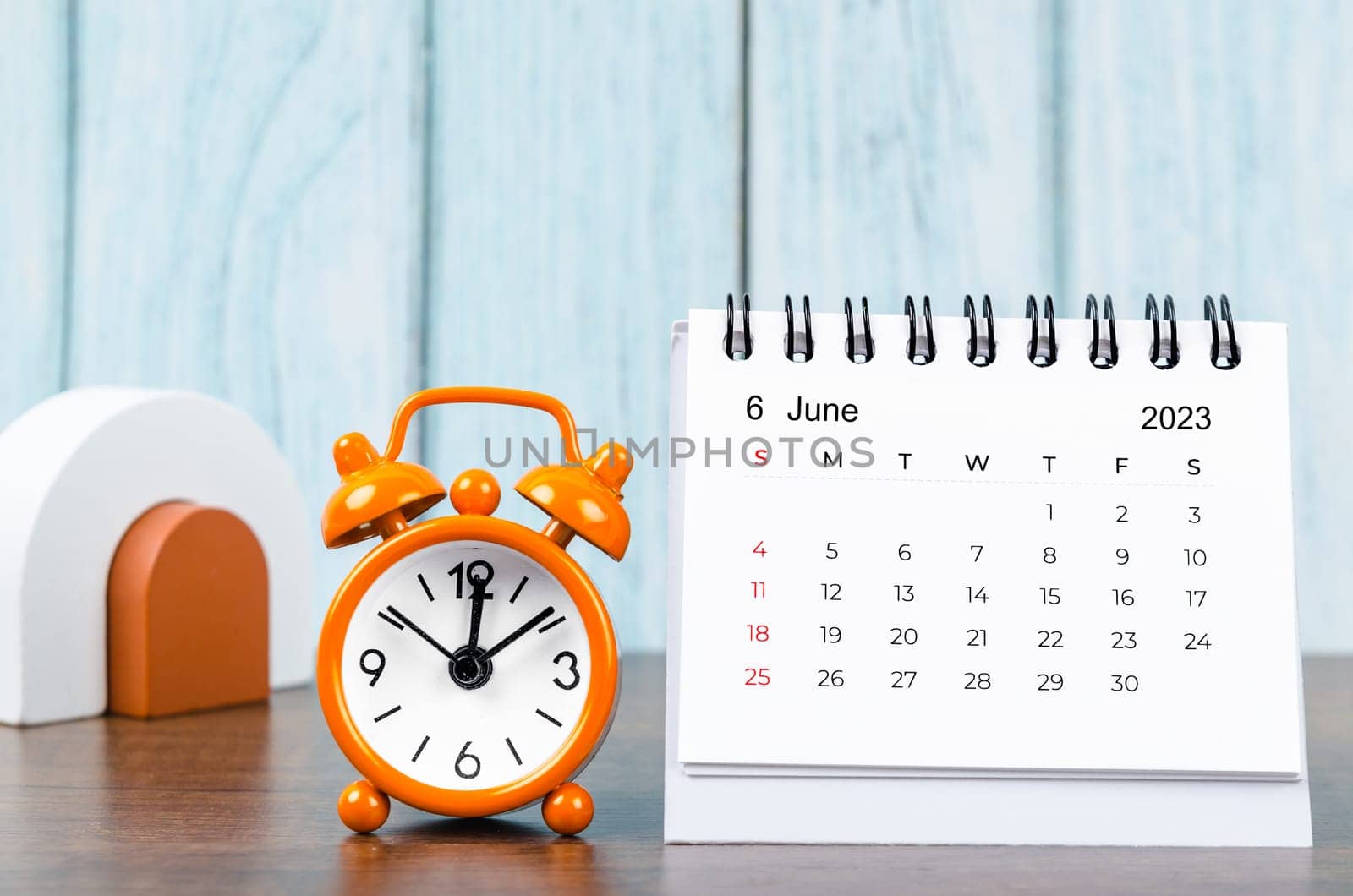 A June 2023 Monthly desk calendar for the organizer to plan 2023 year with alarm clock on wooden table. by Gamjai