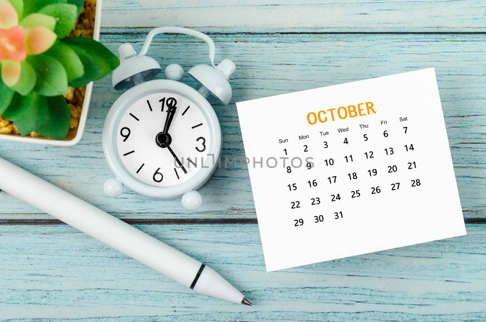 The October 2023 Monthly calendar year and alarm clock with pen on blue wooden background. by Gamjai