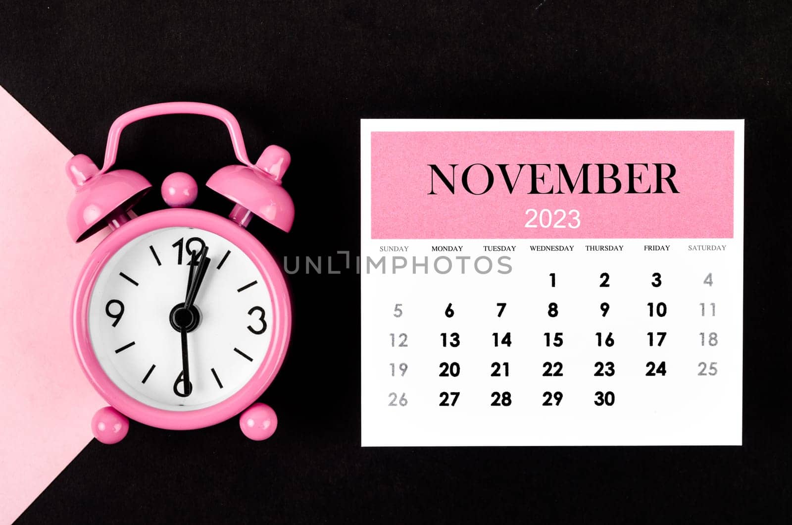 November 2023 Monthly calendar year with alarm clock on pink and black background.