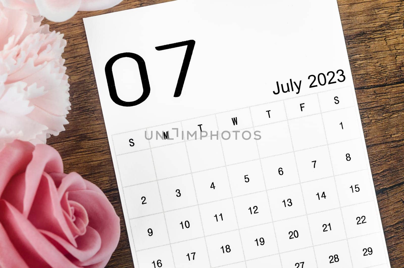 A July 2023 Monthly calendar for 2023 year with pink rose on wooden background. by Gamjai