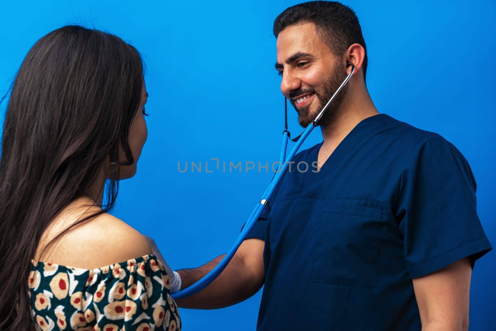 Arab doctor in a blue uniform standing with the stethoscope and listening to the heartbeat of a woman patient, close up