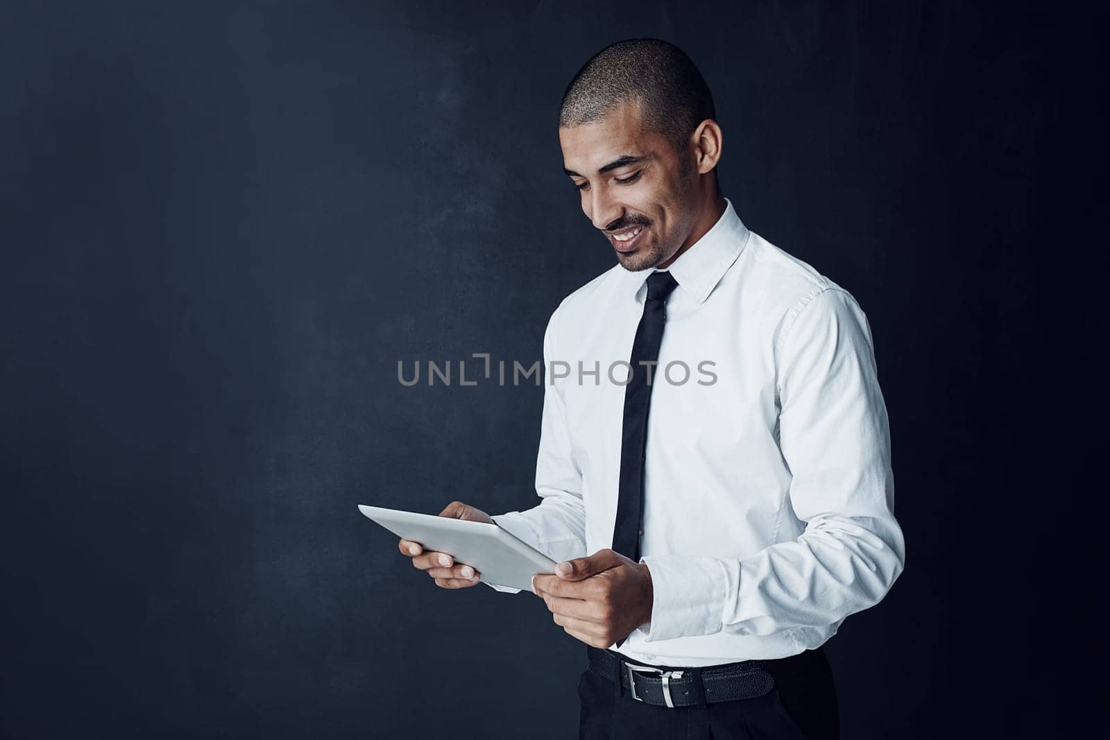 Equipped with smart tools for optimum productivity. Studio shot of a young businessman using a digital tablet against a dark background. by YuriArcurs