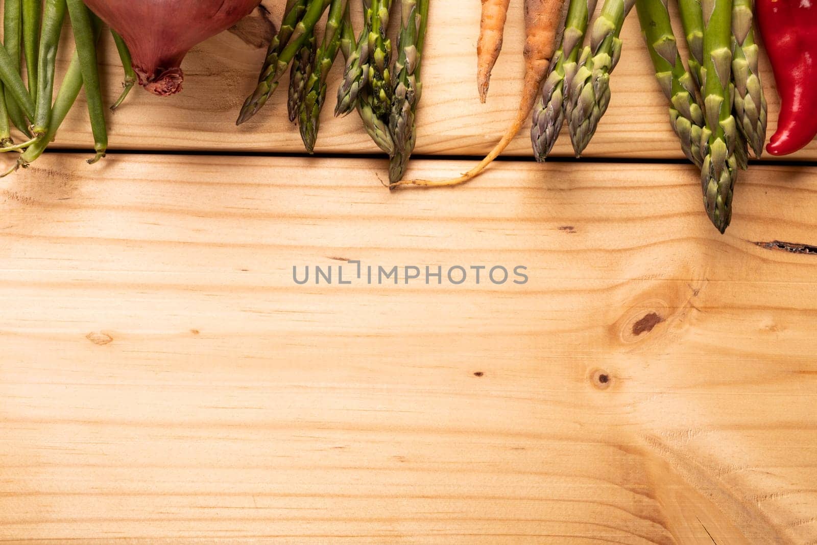 Directly above shot of asparagus with carrots and onion on wooden table with blank space by Wavebreakmedia