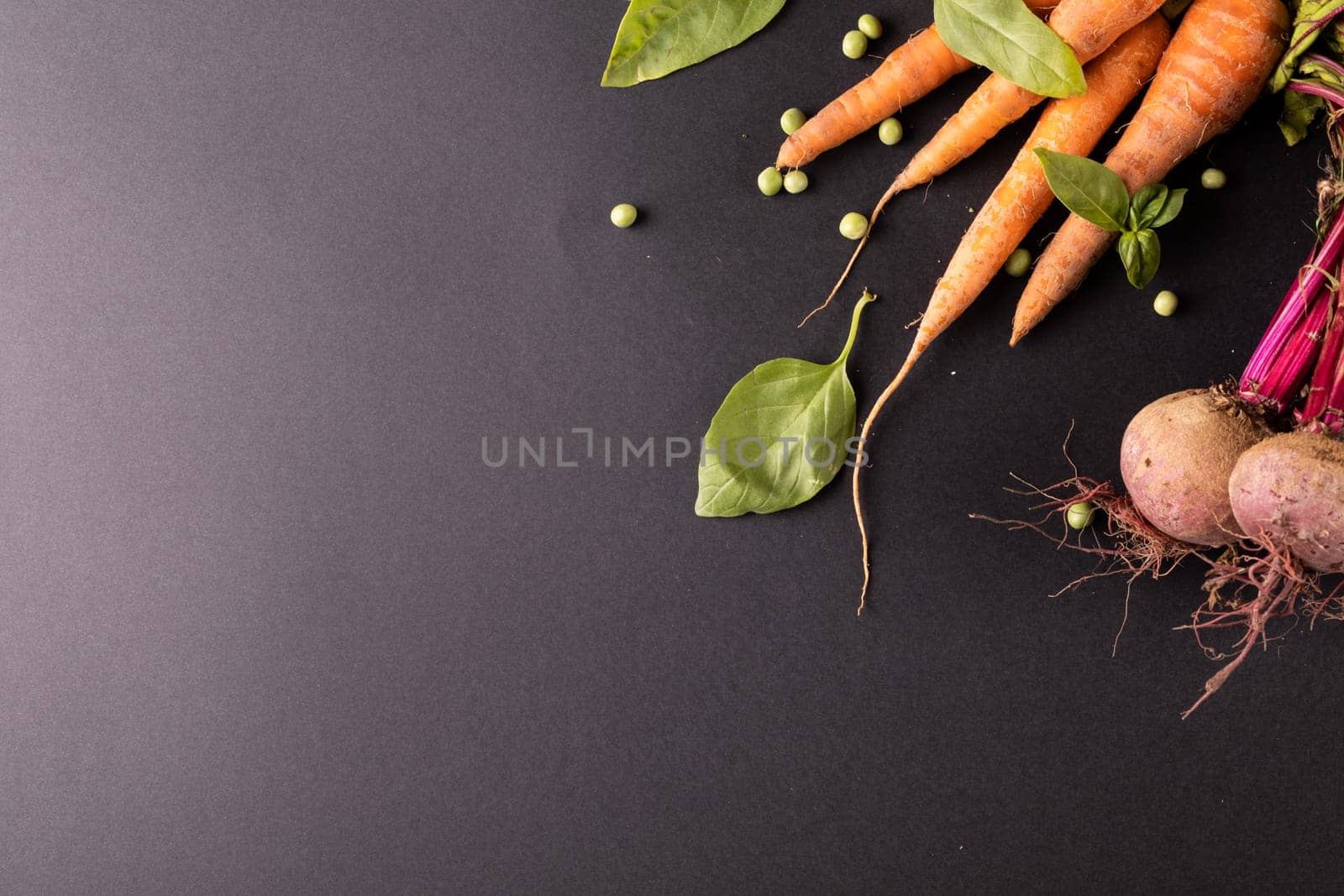 High angle view of carrots and beetroots with green peas and leaf vegetable on black background by Wavebreakmedia