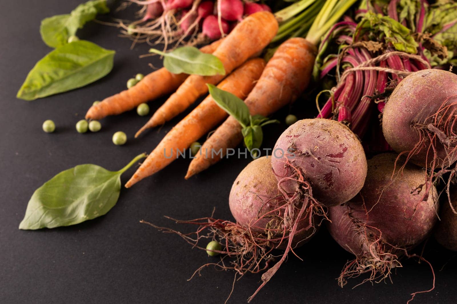 Close-up of carrots and beetroots with green peas and leaf vegetable on black background by Wavebreakmedia