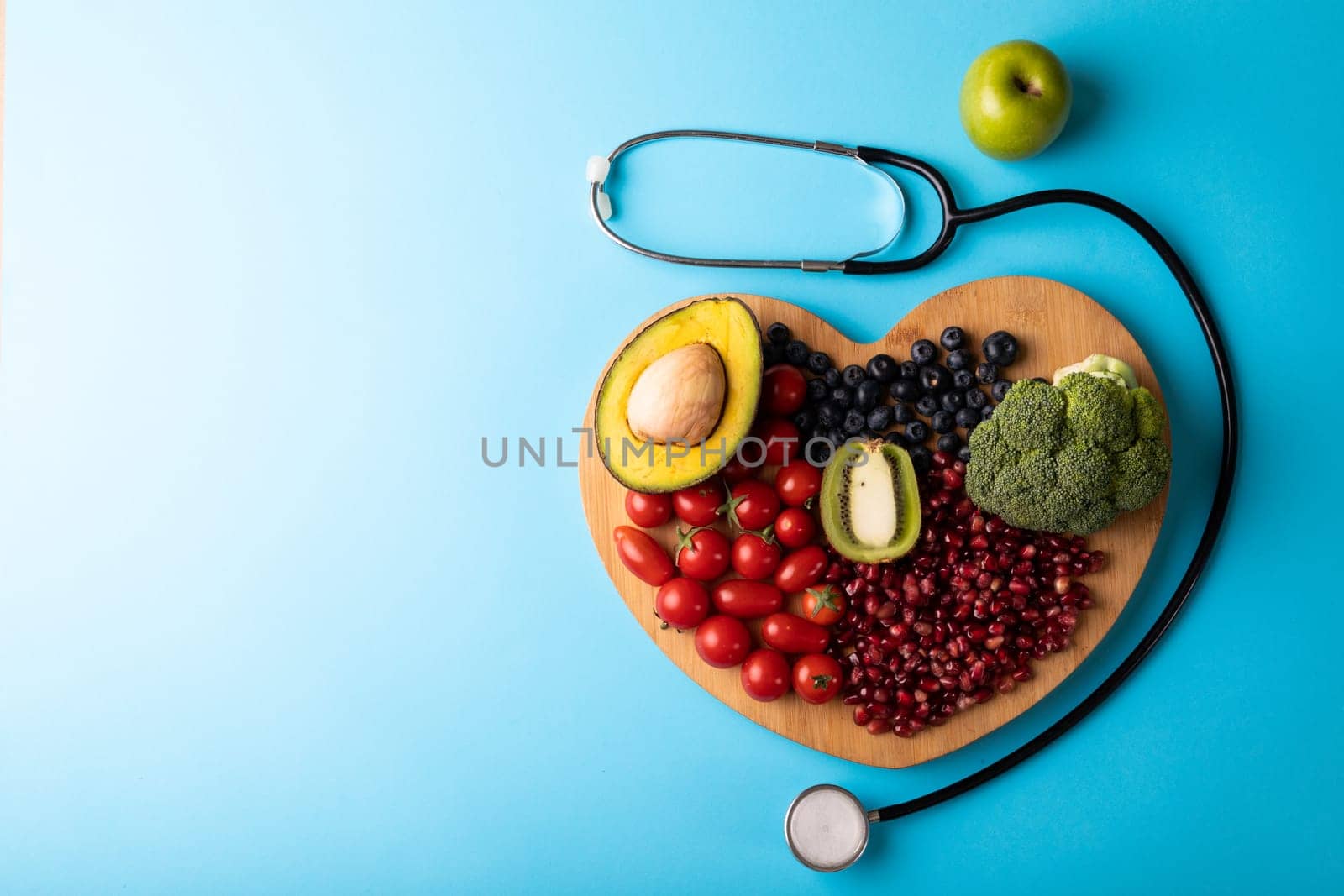 Overhead view of healthy food on heart shaped cutting board by stethoscope on blue background by Wavebreakmedia