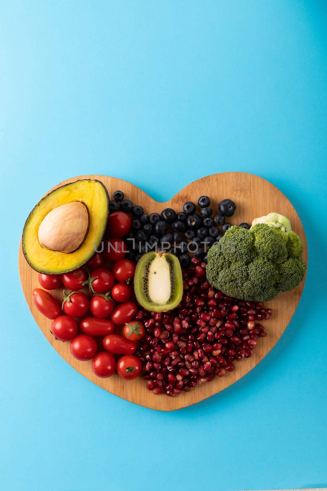 Overhead view of fresh healthy food on heart shaped cutting board over blue background by Wavebreakmedia