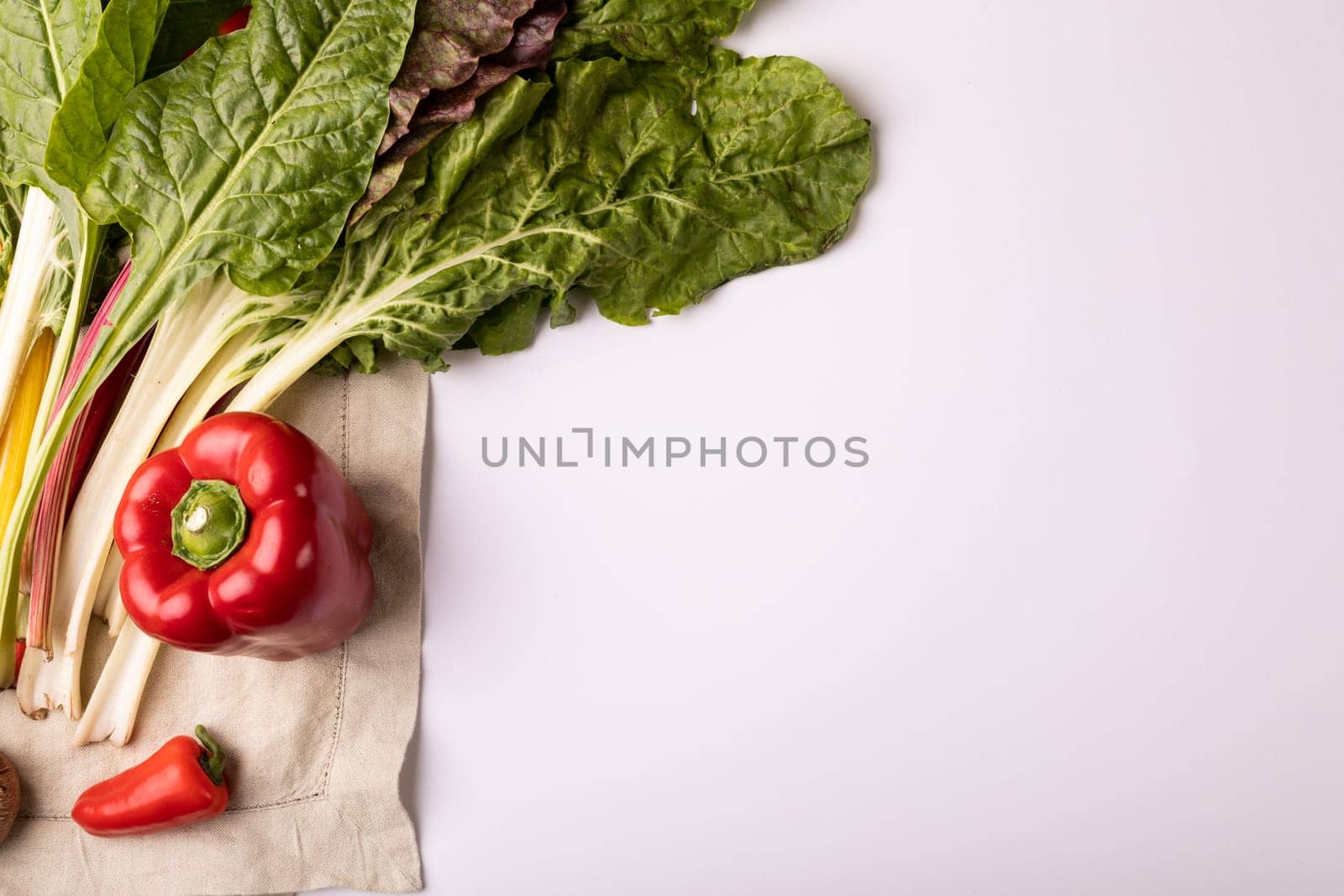 Overhead view of fresh chard with red bell and chili peppers by copy space on white background. unaltered, food, healthy eating, organic concept.