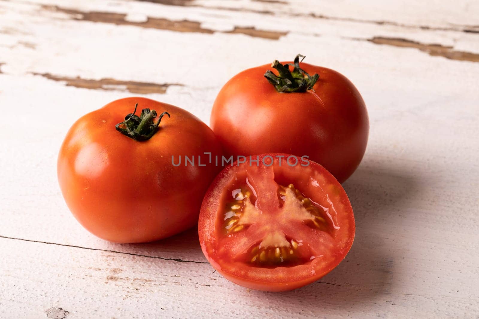 Close-up of fresh red tomatoes and halved on white wooden table by Wavebreakmedia