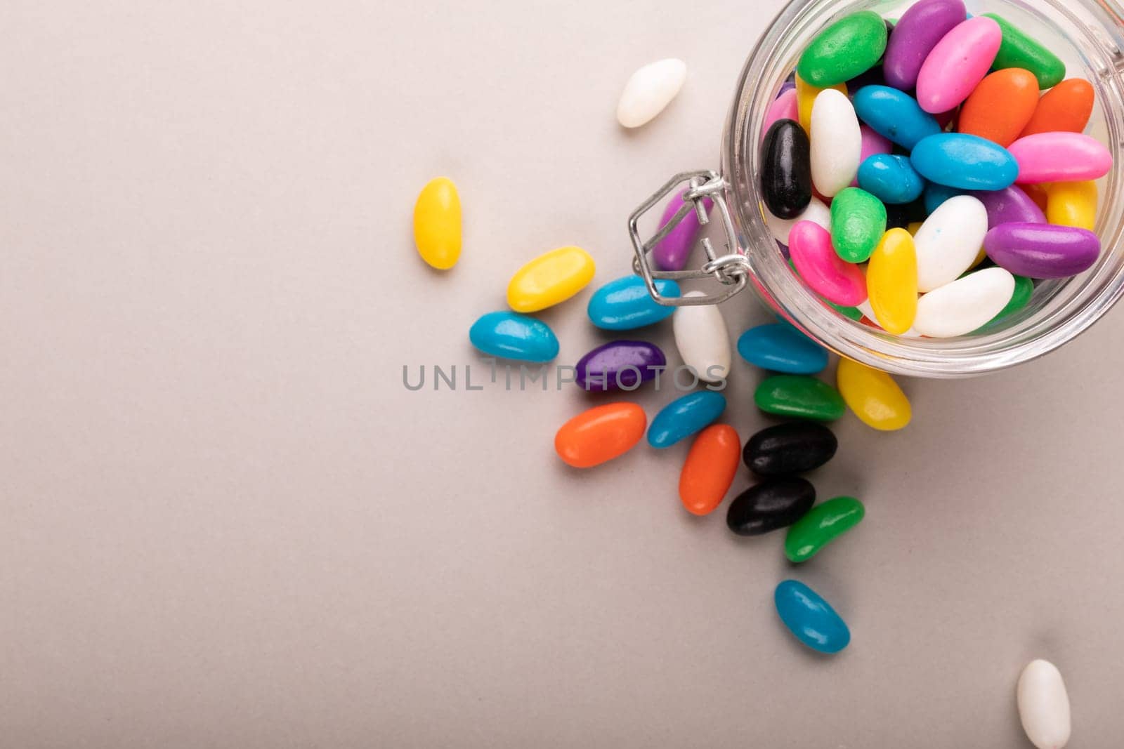 Overhead view of multi colored candies with open glass jar by copy space on white background. unaltered, sweet food and unhealthy eating concept.