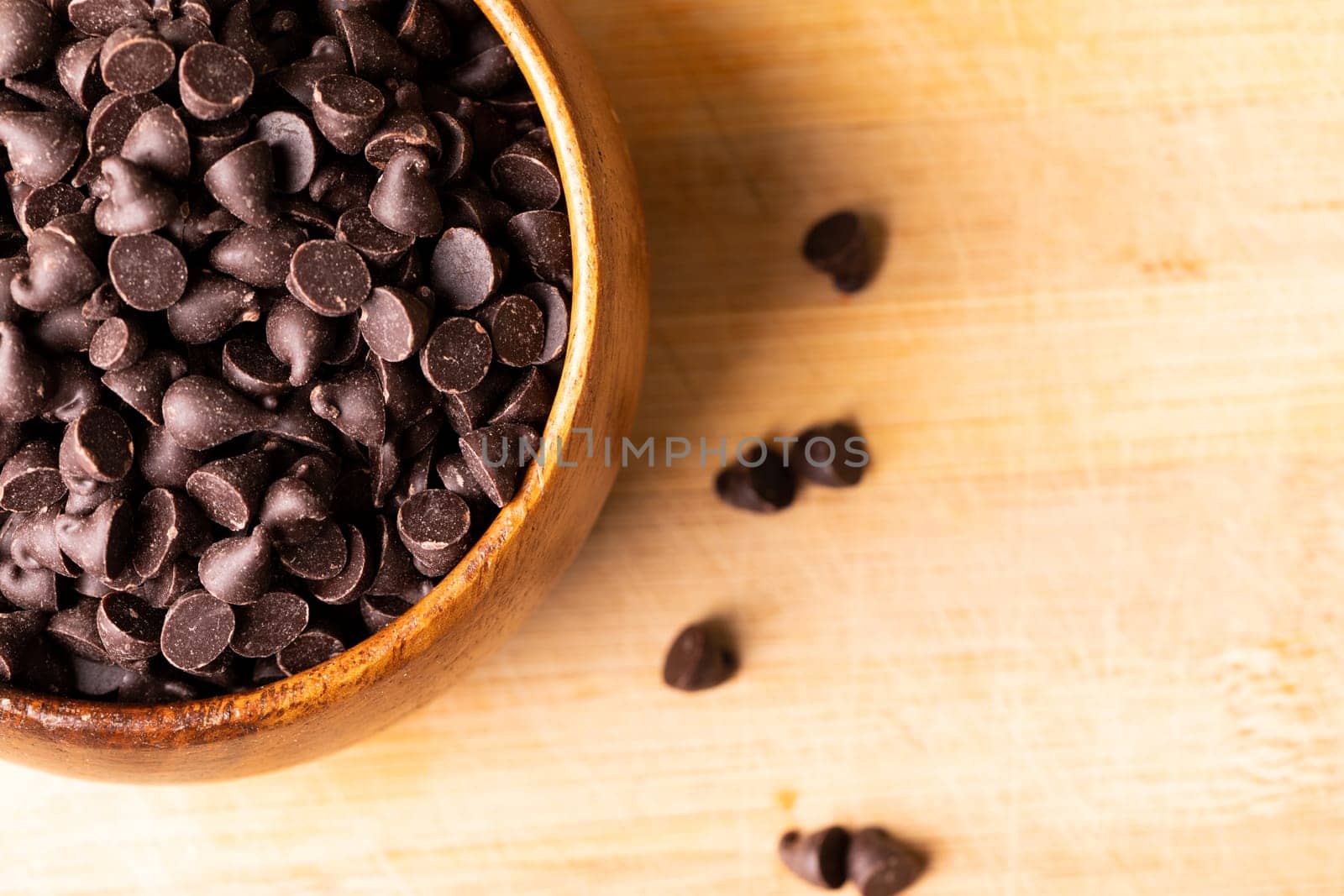Overhead view of chocolate chips in bowl on wooden cutting board. unaltered, sweet food and unhealthy eating concept.