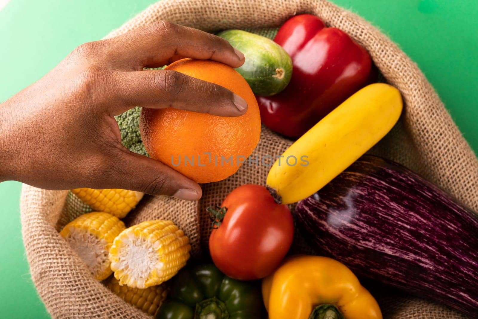 Cropped hand of mixed race man holding fresh orange fruit over vegetables in burlap sack by Wavebreakmedia