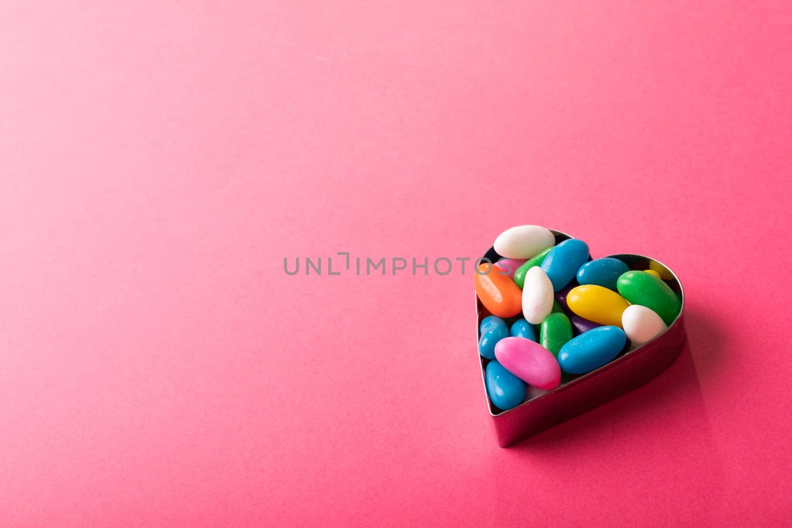 High angle view of multi colored candies in heart shape container by copy space on pink background by Wavebreakmedia