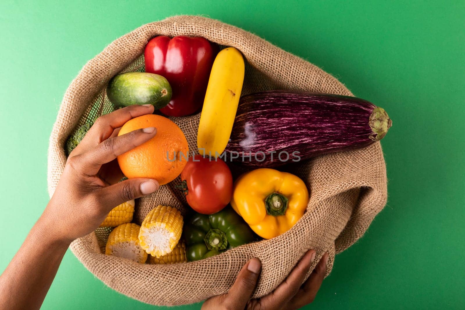 Directly above view of mixed race man hand holding fresh orange fruit over vegetables in burlap sack by Wavebreakmedia