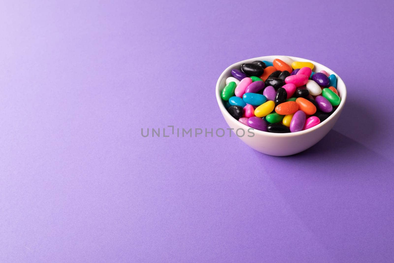 High angle view of multi colored candies in bowl on purple background with copy space. unaltered, sweet food and unhealthy eating concept.