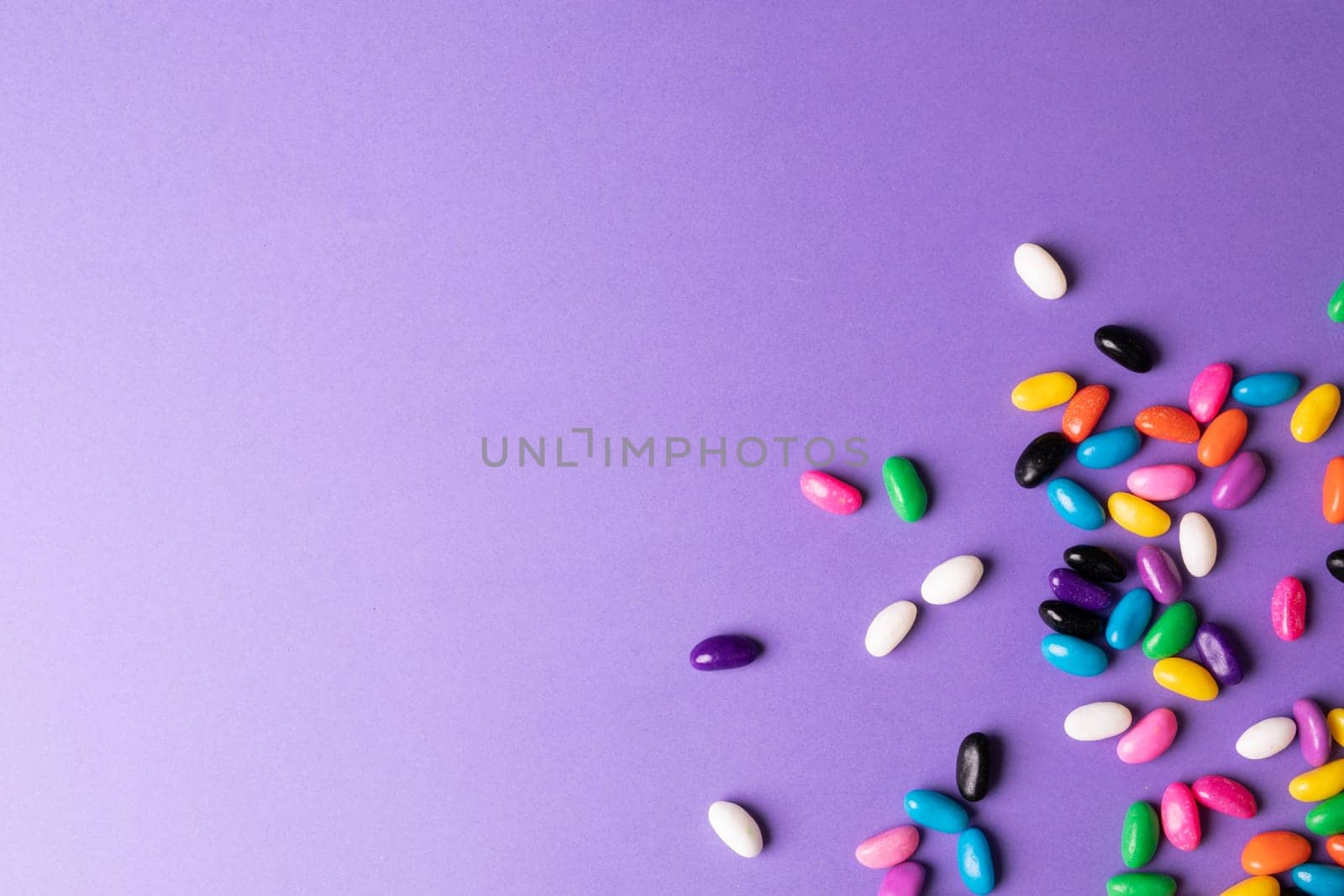 Directly above view of scatted multi colored candies on purple background with copy space. unaltered, sweet food and unhealthy eating concept.