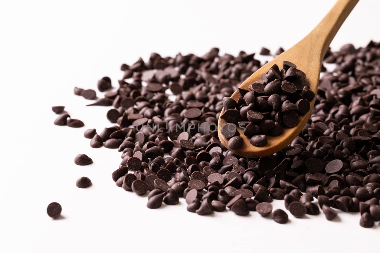 Close-up of wooden spoon with chocolate chips against white background. unaltered, sweet food and unhealthy eating concept.