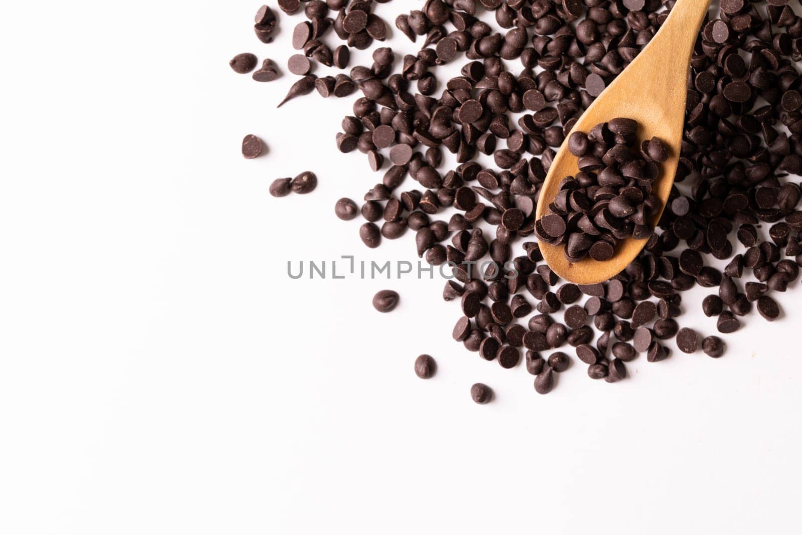 Overhead view of wooden spoon over fresh chocolate chips on white background with copy space by Wavebreakmedia