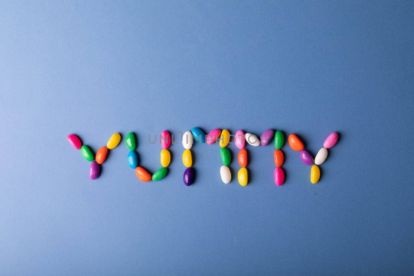 Overhead view of multi colored candies arranged as yummy word on blue background with copy space by Wavebreakmedia
