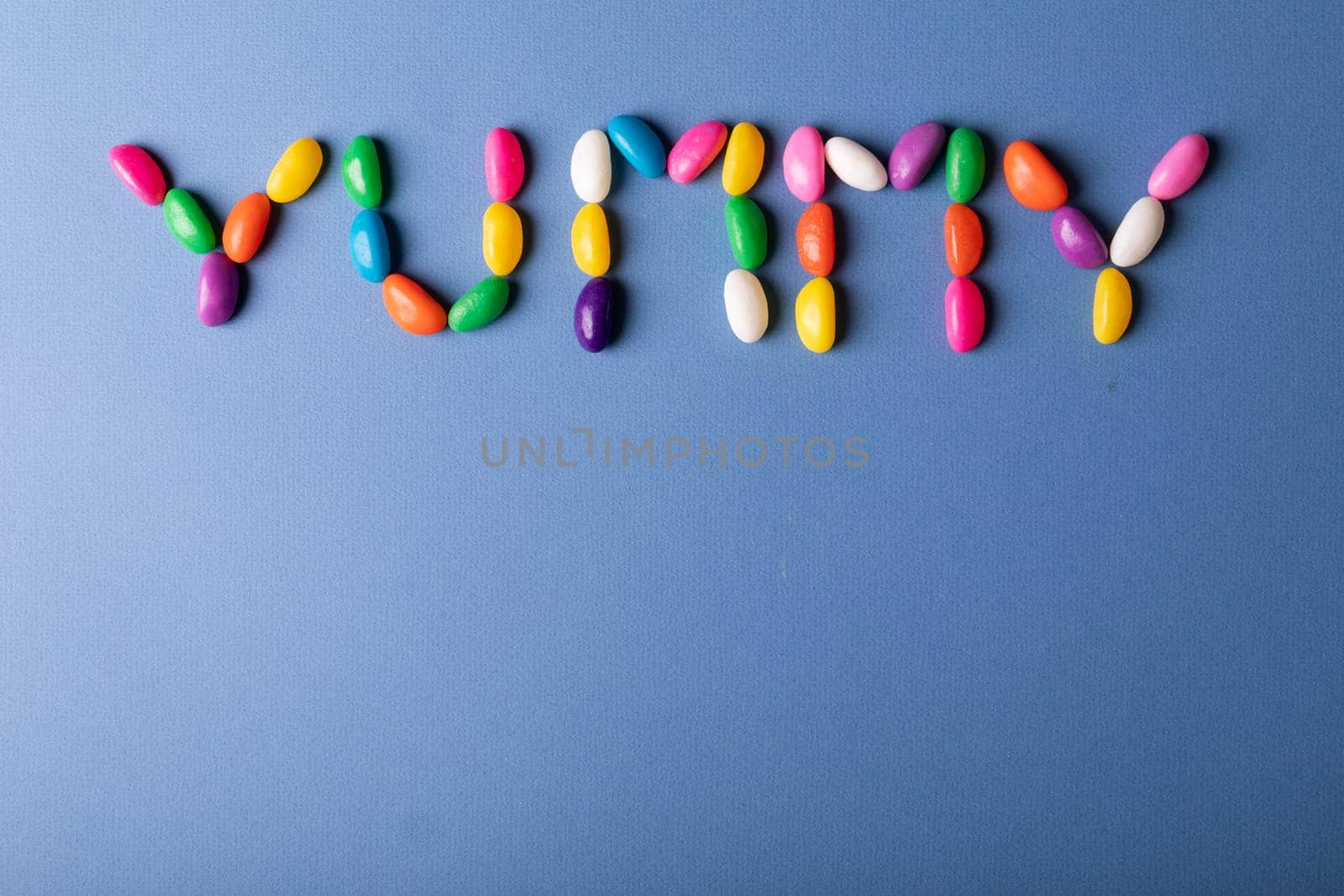 Overhead view of yummy word arranged from multi colored candies on blue background over copy space. unaltered, sweet food and unhealthy eating concept.