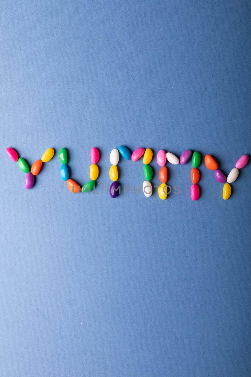 Directly above view of yummy word arranged from colorful candies on blue background over copy space. unaltered, sweet food and unhealthy eating concept.