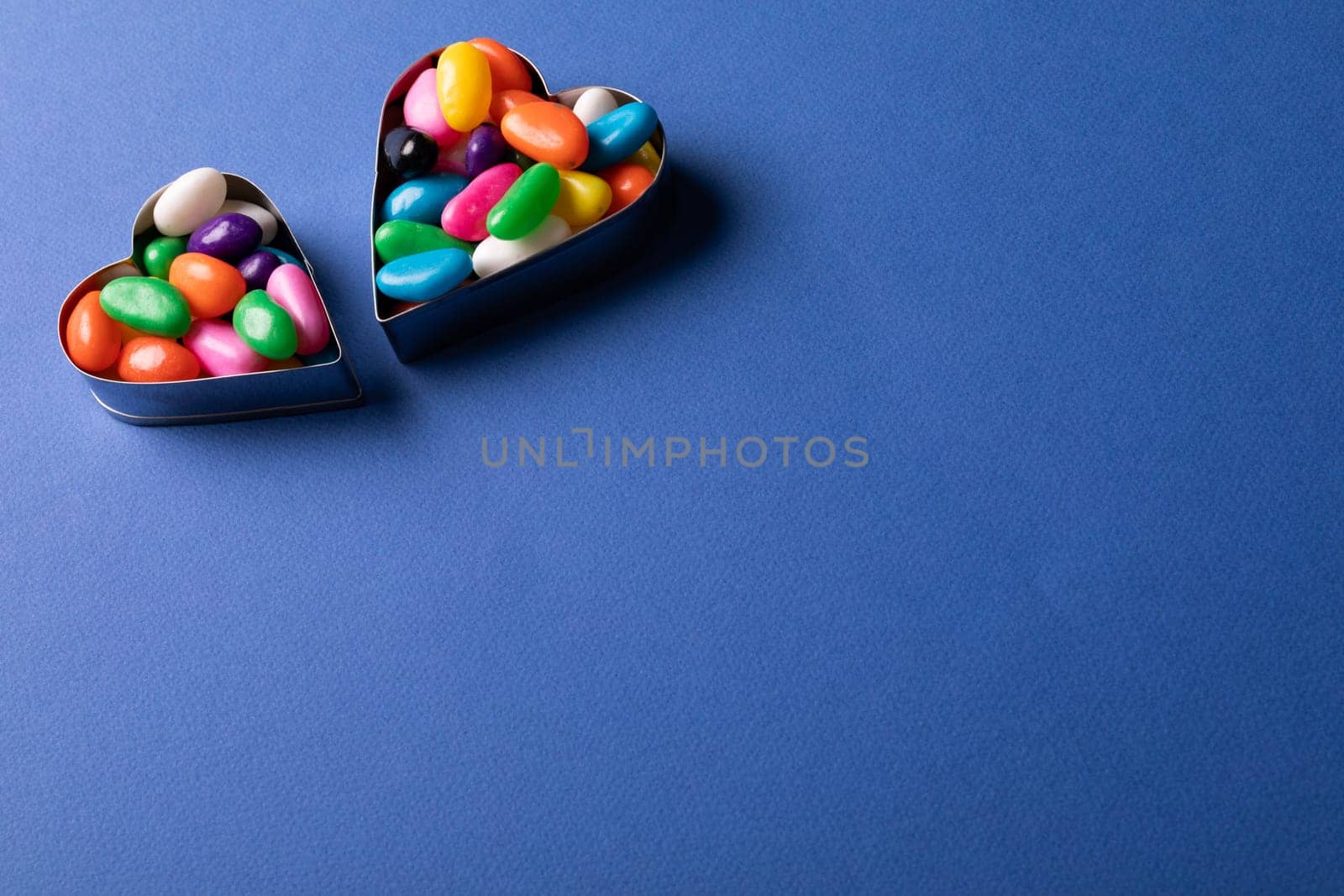 High angle view of heart shape containers with colorful candies by copy space on blue background by Wavebreakmedia