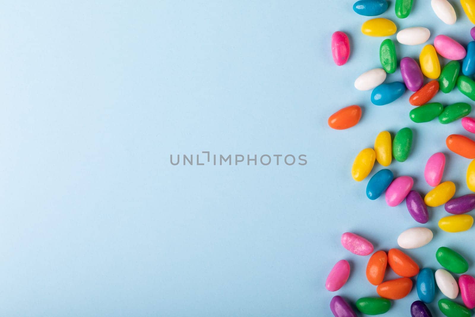 Overhead view of scattered multi colored candies by copy space over blue background. unaltered, sweet food and unhealthy eating concept.