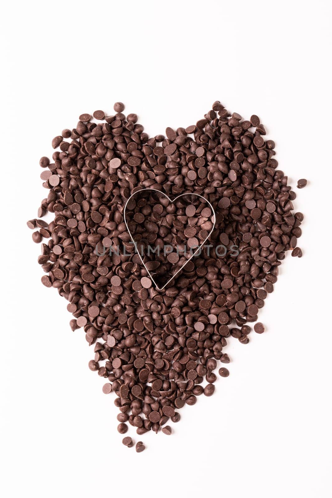 Overhead view of heart shape pastry cutter over chocolate chips on white background. unaltered, sweet food and unhealthy eating concept.