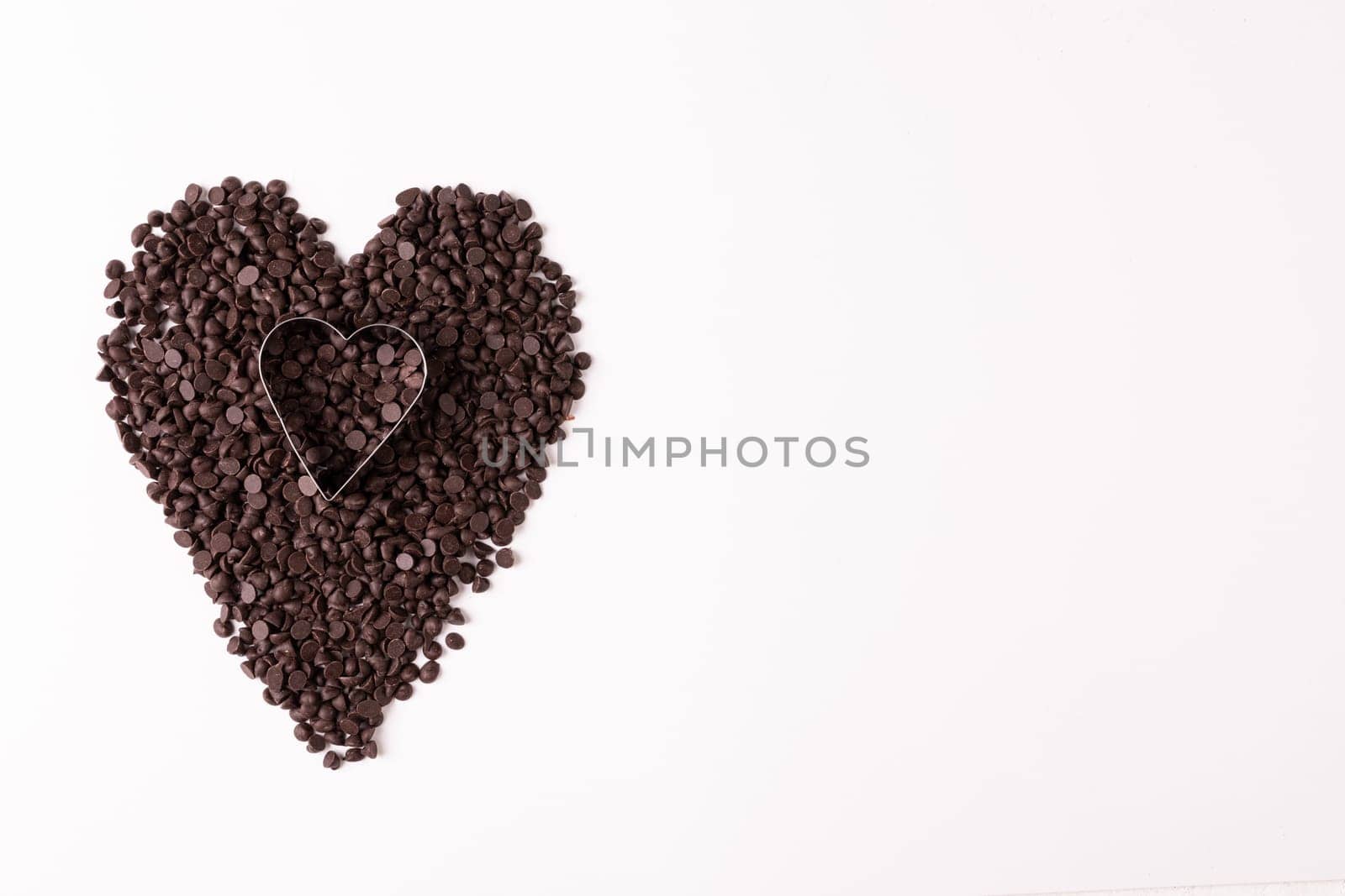 Overhead view of heart shape pastry cutter on chocolate chips by copy space over white background. unaltered, sweet food and unhealthy eating concept.