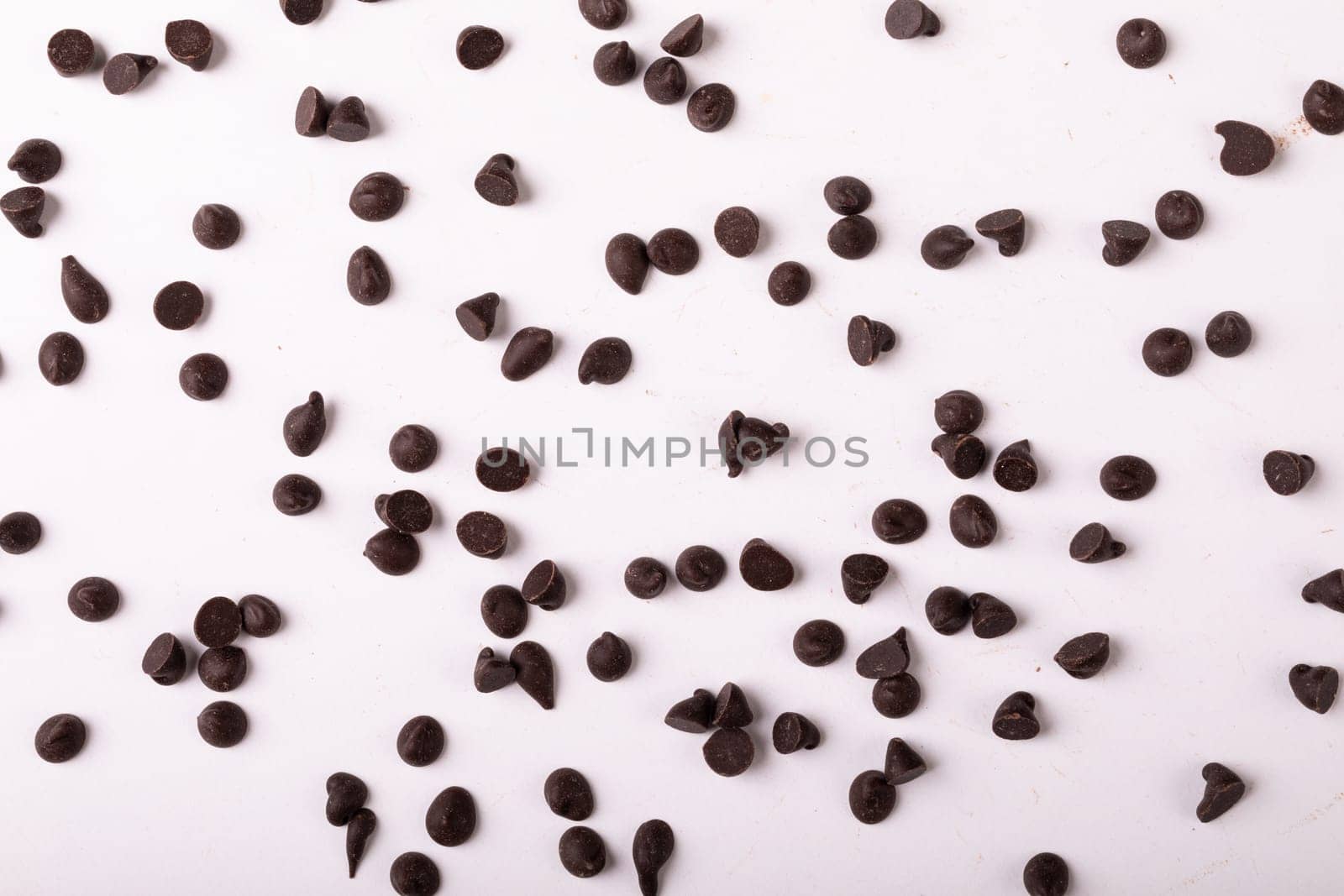 Full frame shot of fresh chocolate chips scattered over white background. unaltered, sweet food and unhealthy eating concept.