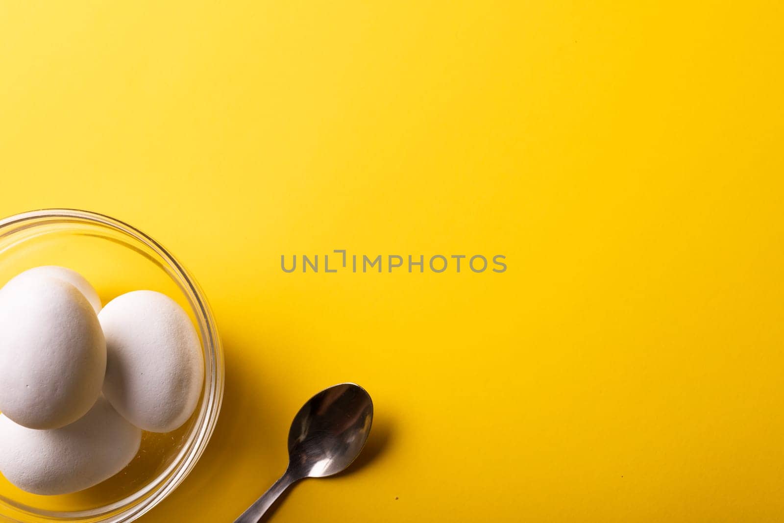 Overhead view of fresh white eggs in bowl by spoon and copy space on yellow background by Wavebreakmedia