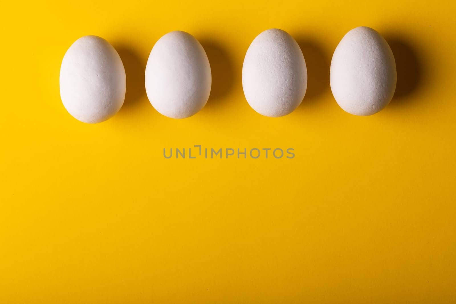 Overhead view of fresh white eggs arranged side by side on yellow background with copy space. unaltered, food, healthy eating concept.