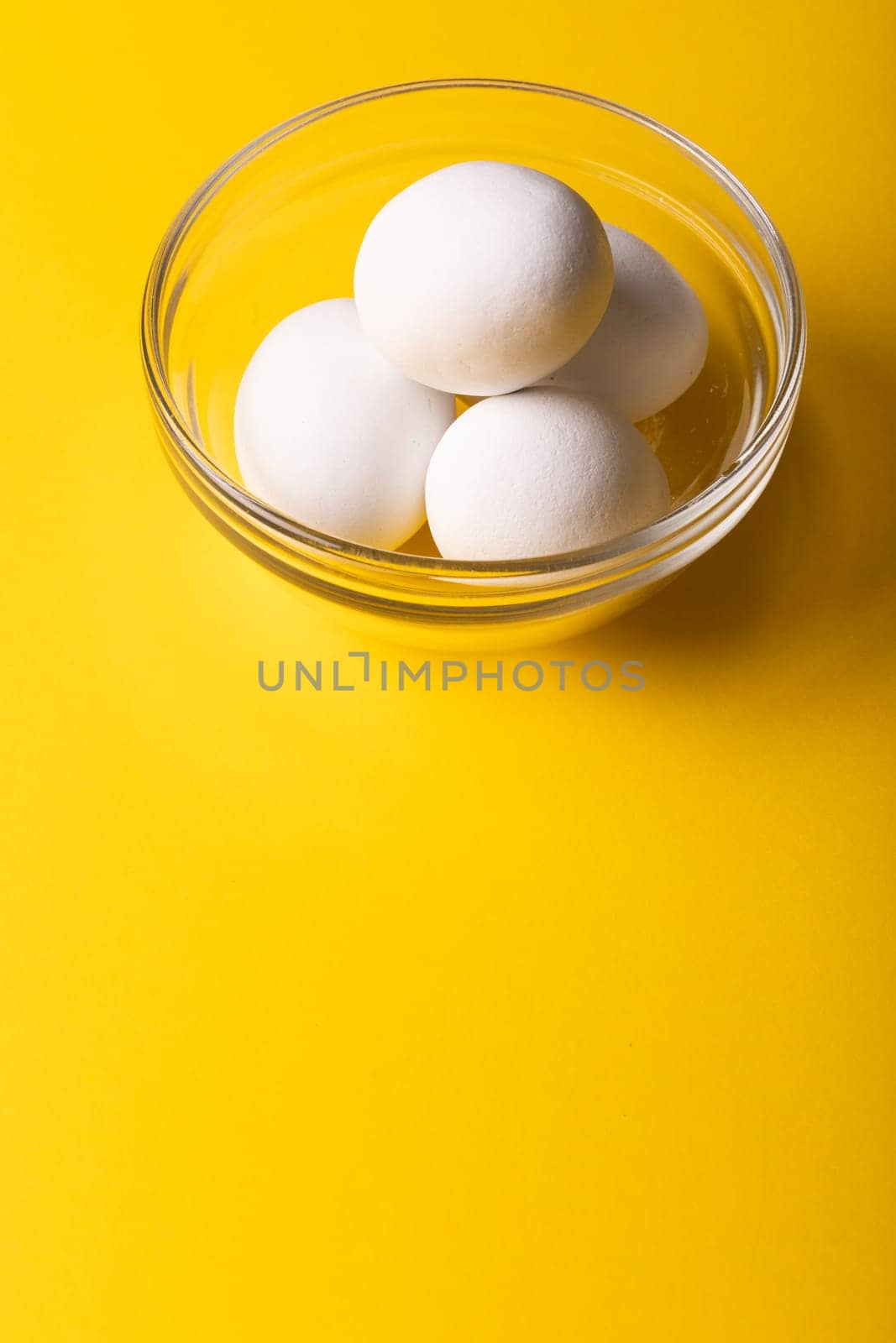 High angle view of fresh white eggs in glass bowl over yellow background with copy space. unaltered, food, healthy eating concept.