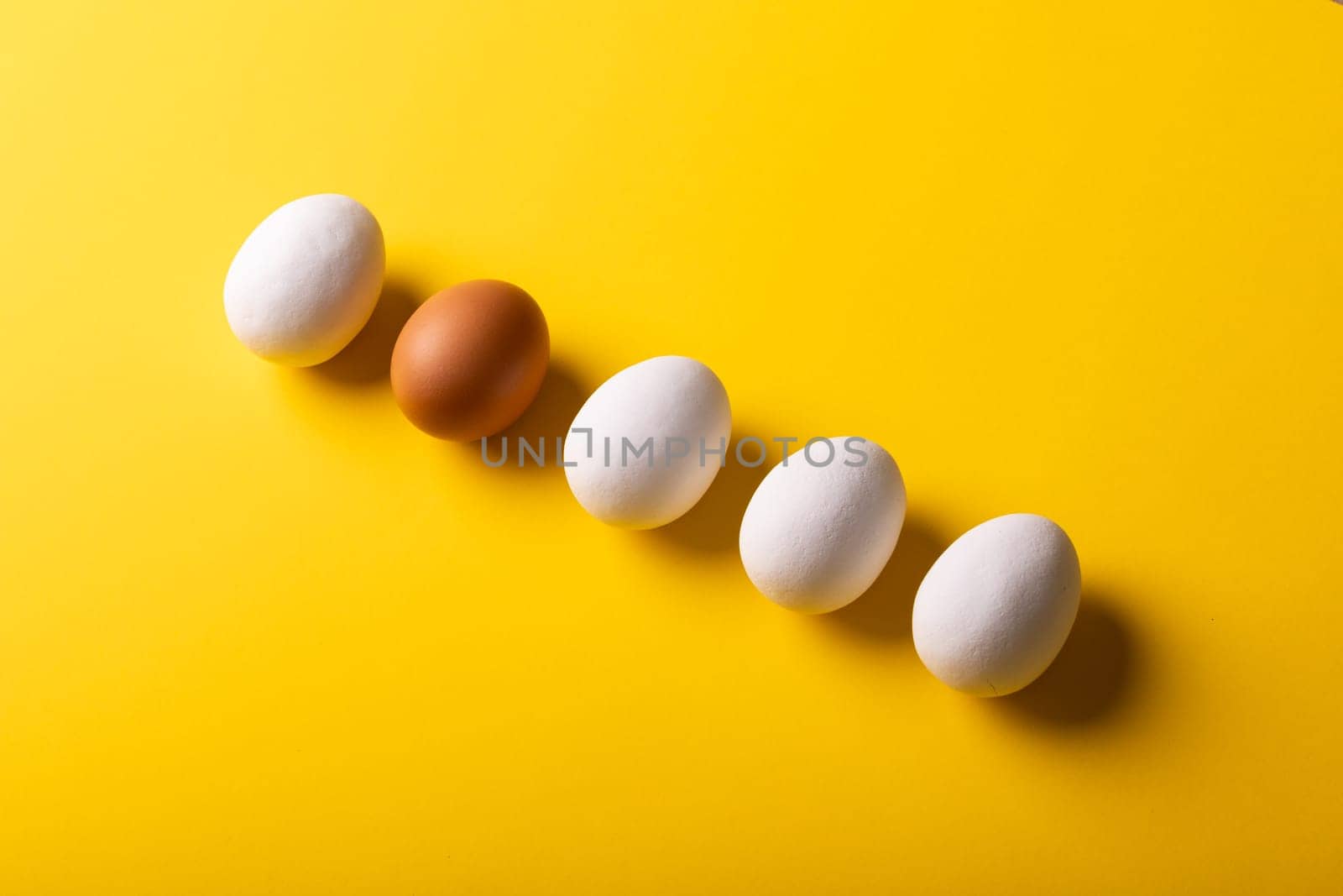 High angle view of brown and white eggs arranged side by side on yellow background with copy space. unaltered, food, healthy eating concept.
