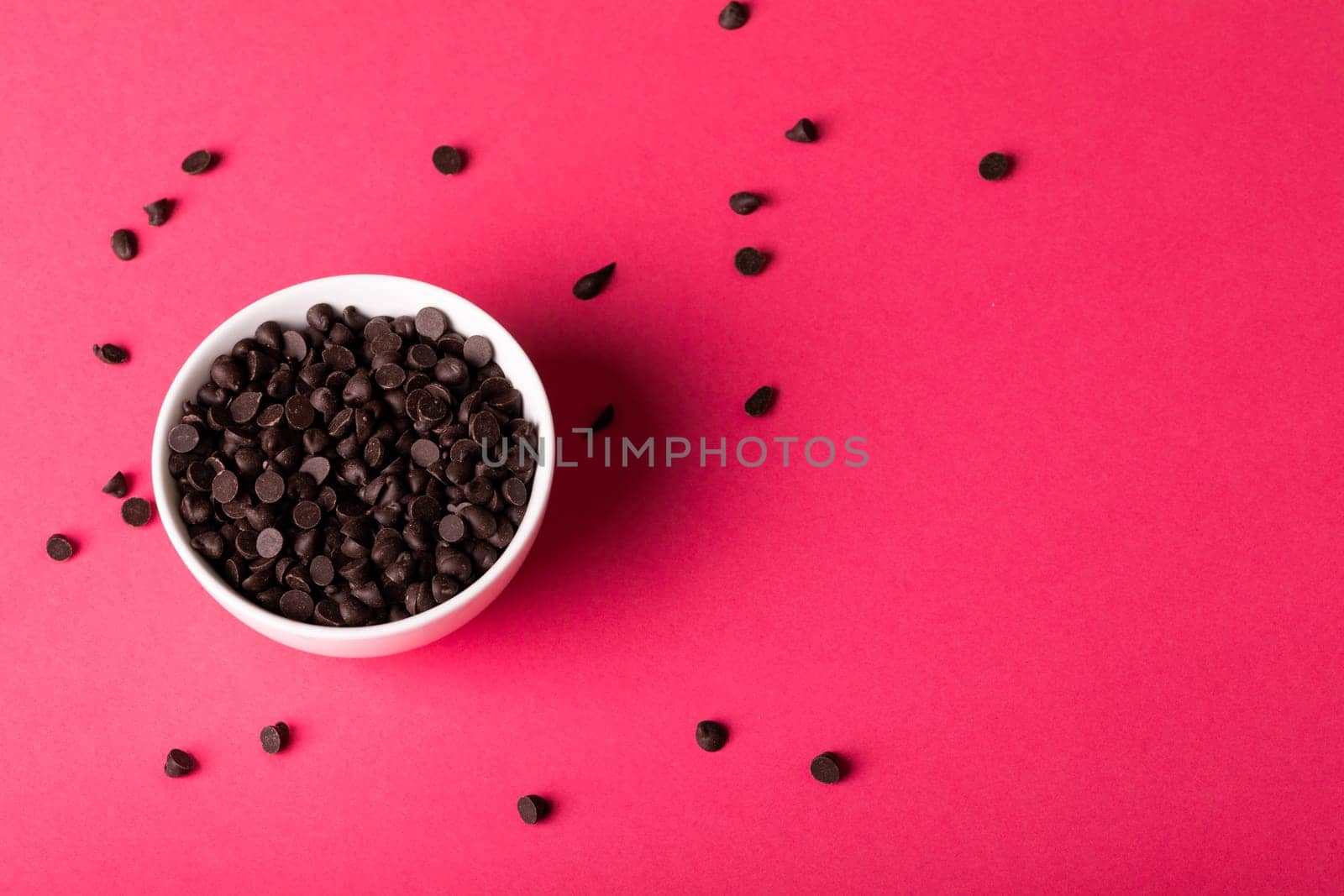 Directly above view of bowl with fresh chocolate chips scattered by copy space over pink background. unaltered, sweet food and unhealthy eating concept.