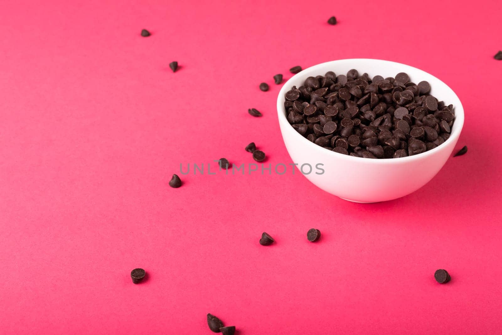 High angle view of fresh chocolate chips full of white bowl against pink background by Wavebreakmedia