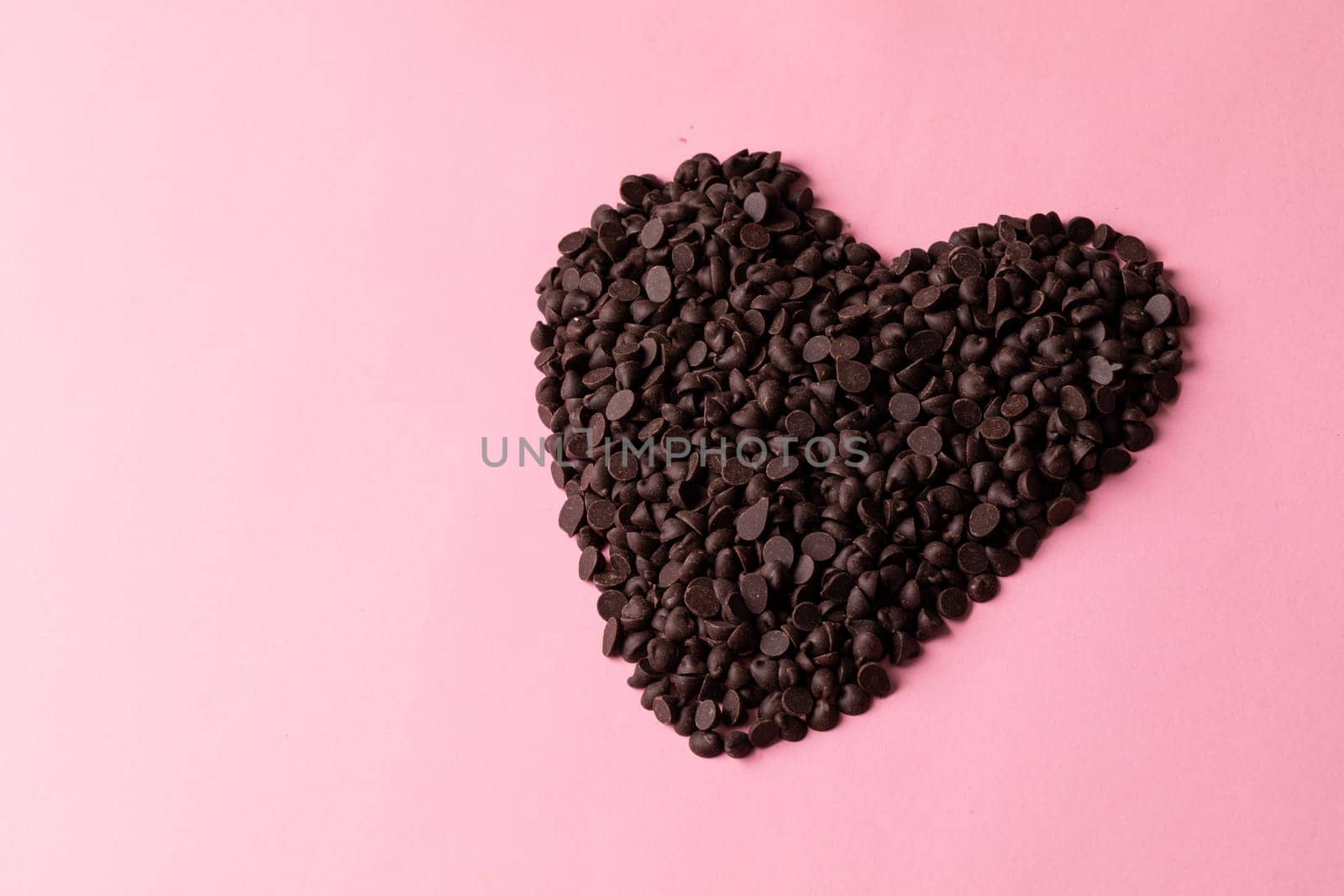 High angle view of fresh chocolate chips arranged heart shape by copy space against pink background. unaltered, sweet food and unhealthy eating concept.