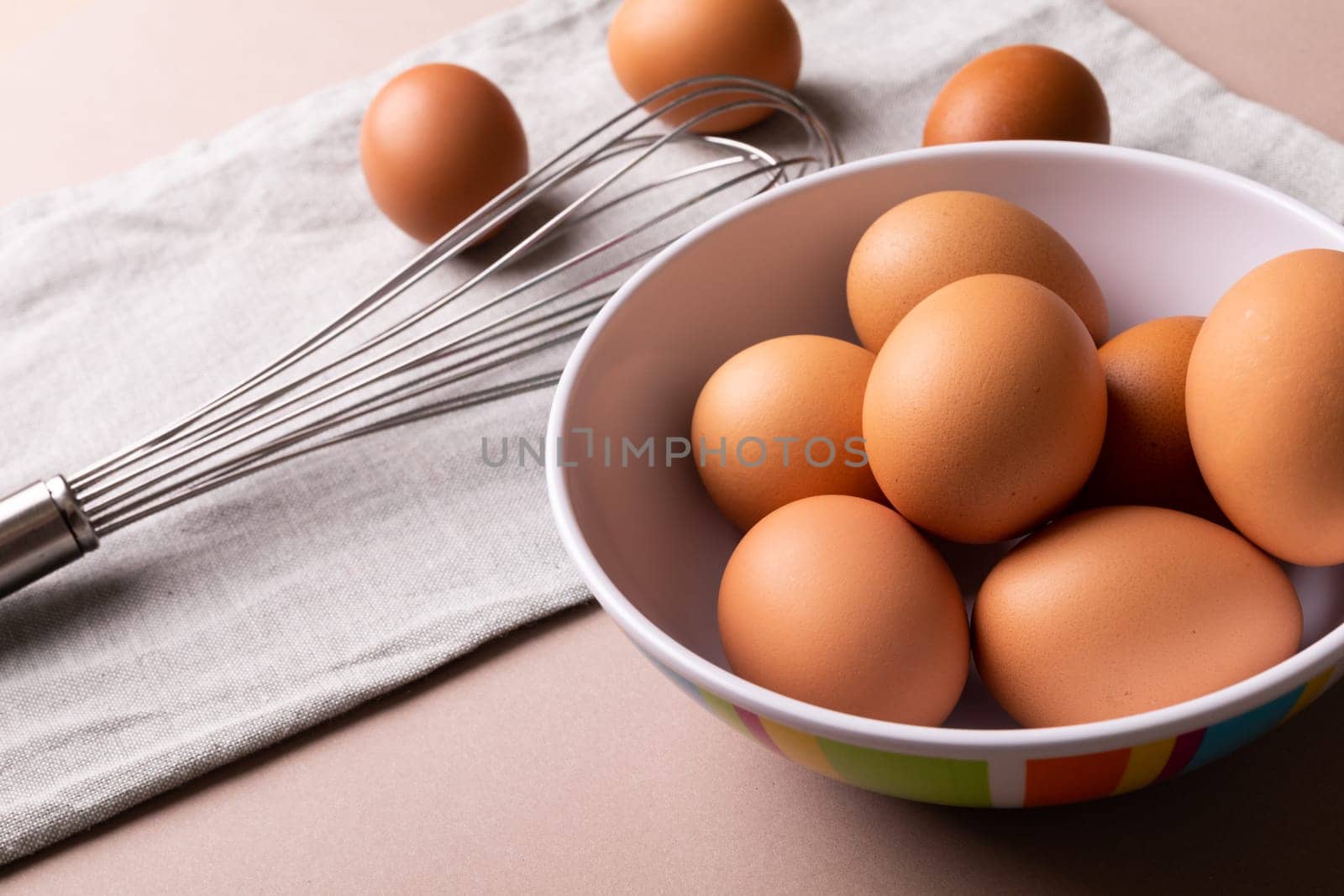 High angle view of fresh brown eggs in bowl by wire whisk on napkin by Wavebreakmedia