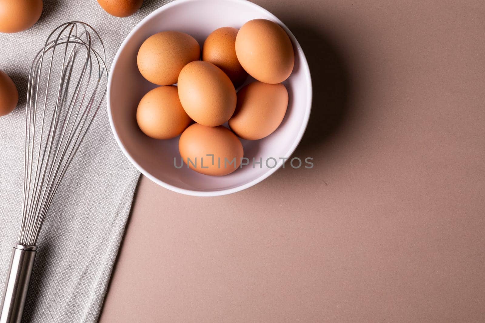 Overhead view of fresh brown eggs in bowl by wire whisk on table with copy space. unaltered, food, healthy eating concept.