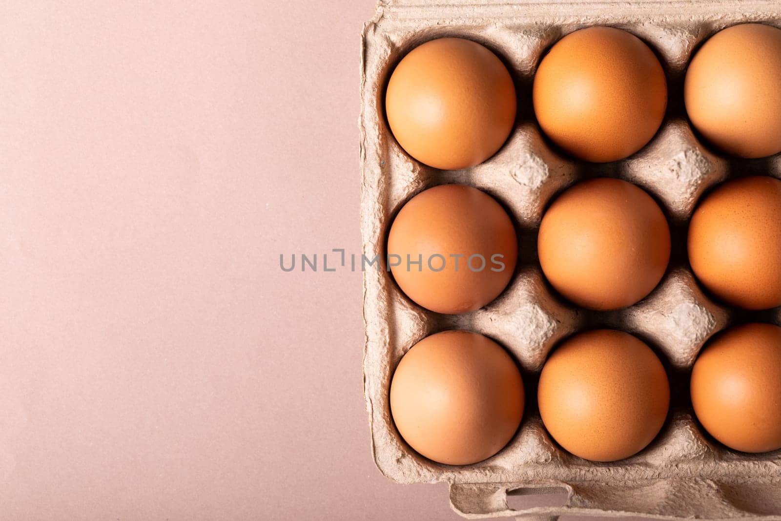 Directly above view of fresh brown eggs in carton by copy space on colored background by Wavebreakmedia