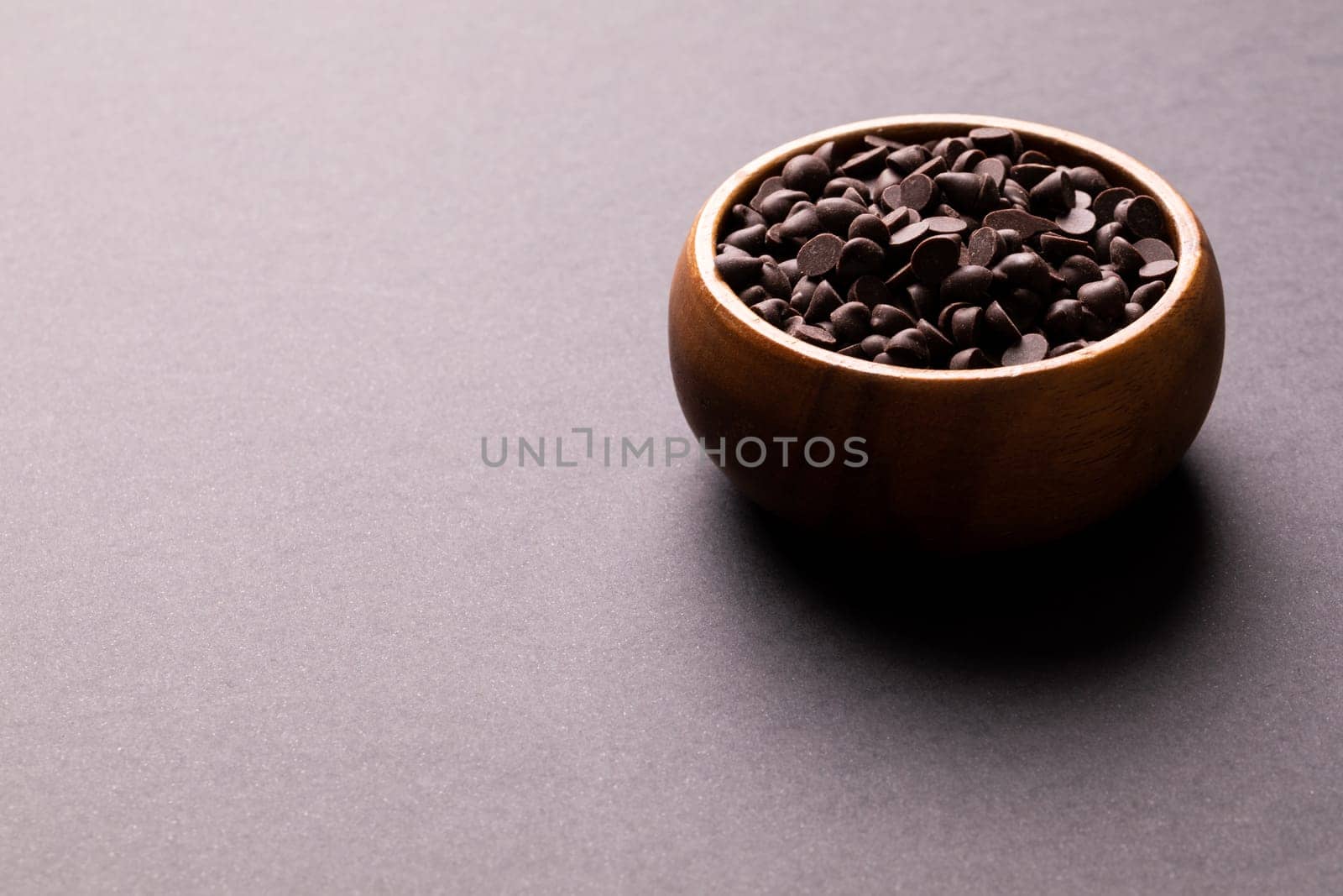 High angle view of fresh chocolate chips in wooden bowl against colored background with copy space by Wavebreakmedia