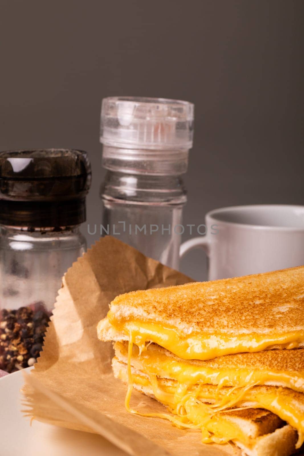 Close-up of fresh cheese sandwich on wax paper by peppercorn bottle and cup against gray background by Wavebreakmedia